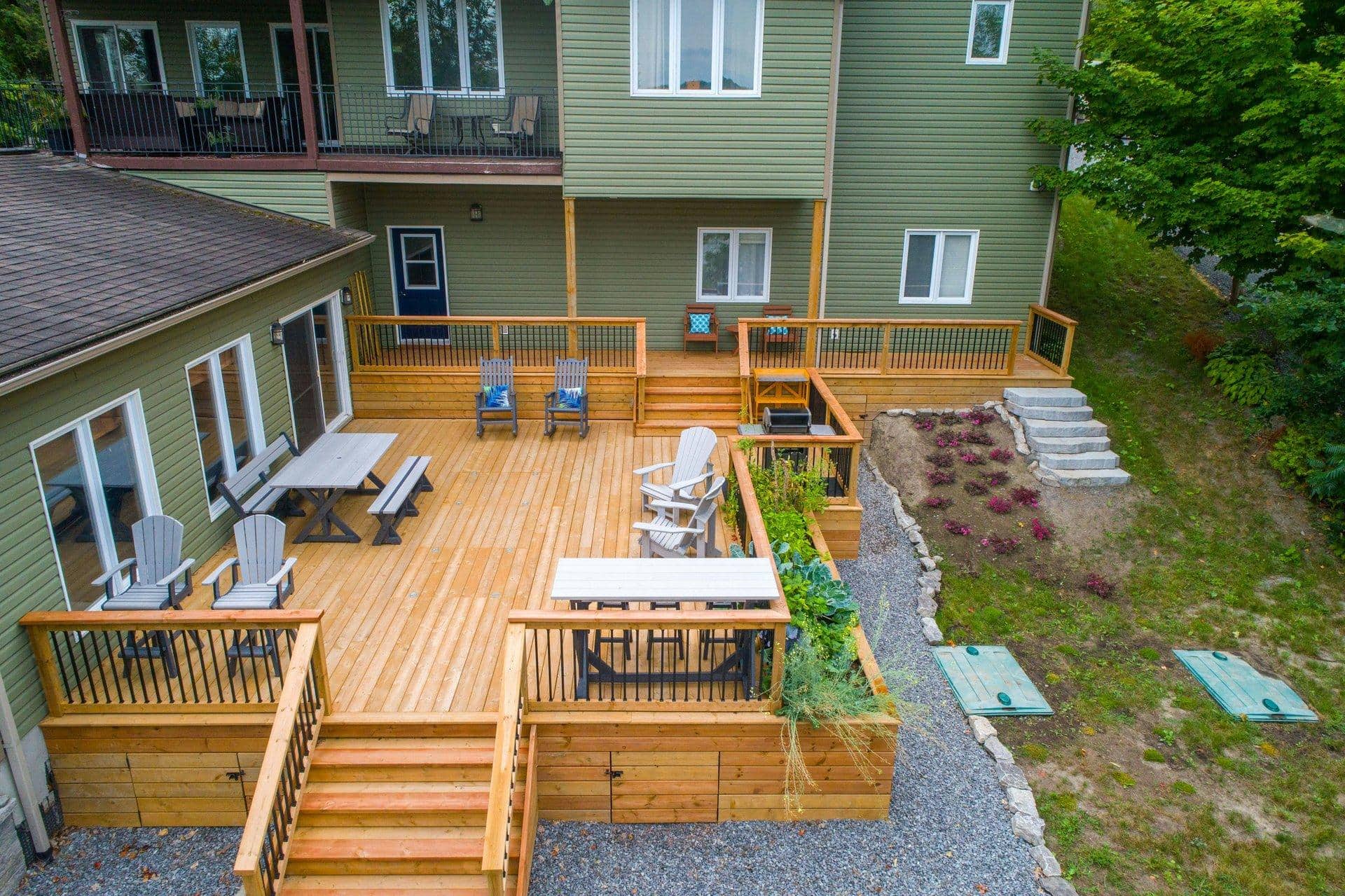A clean, well-maintained wood deck behind a residential home on a sunny spring afternoon, with patio furniture and a few potted plants