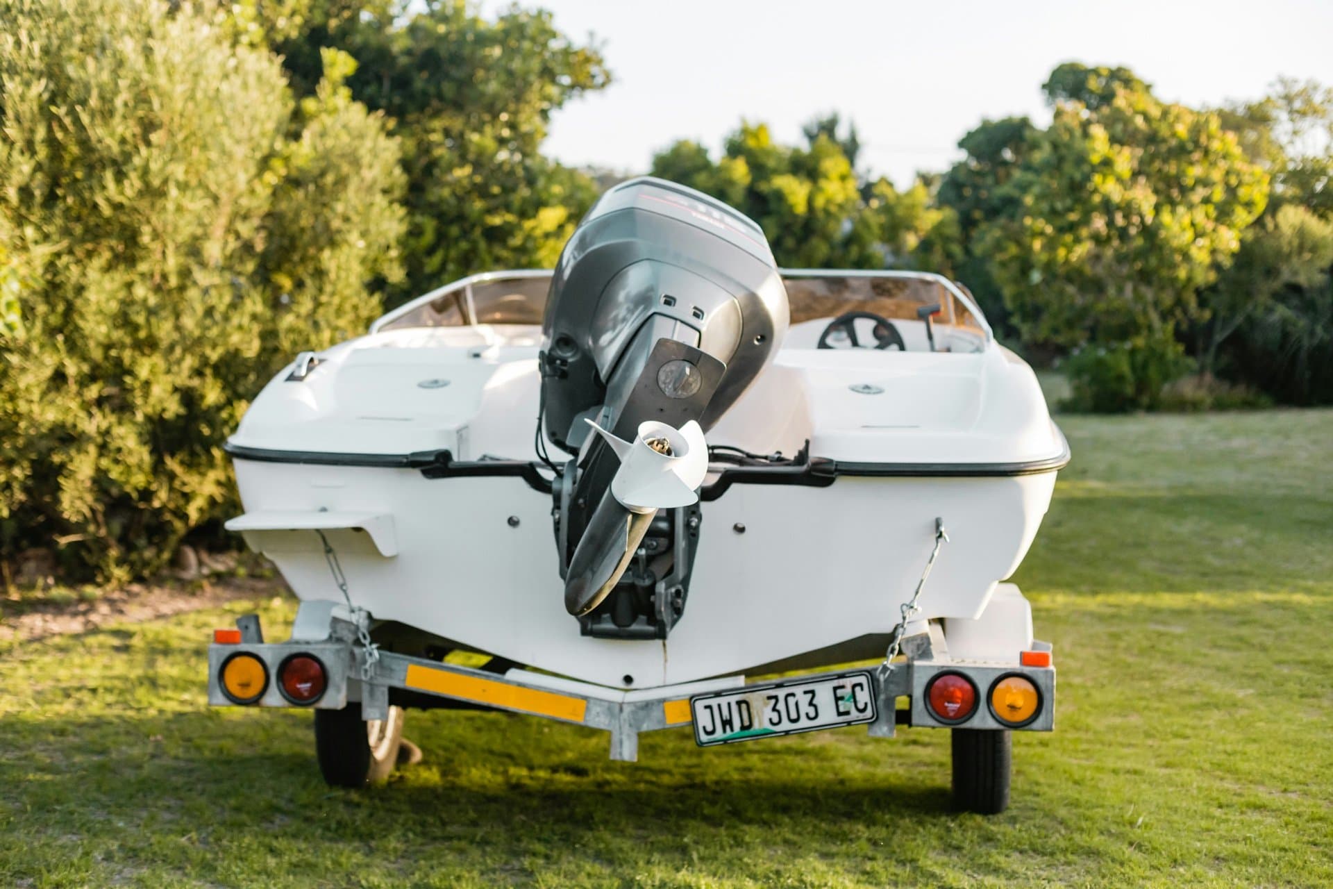 A trailered boat in a residential driveway on a bright spring morning, ready for launch with calm water visible in the background